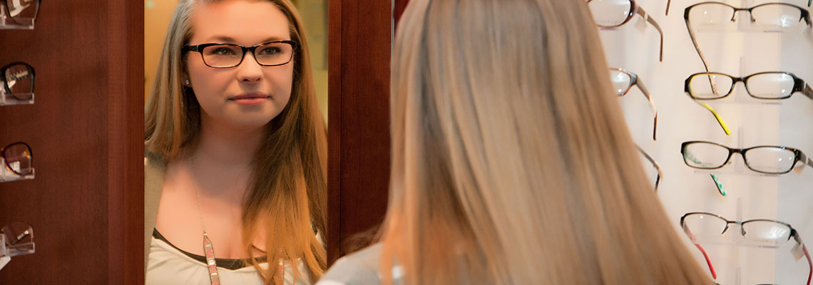 Girl looking in the mirror while trying out new glasses at Eye & Vision Clinics, S.C.